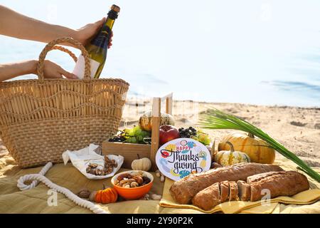 Woman having picnic with wine, delicious food and Thanksgiving Day greeting card on beach Stock Photo