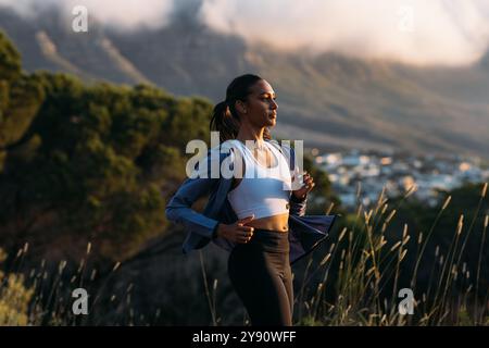 Confident female runner practicing outdoors at stunning sunset. Side view of slim woman in fitness attire jogging at sunset. Stock Photo