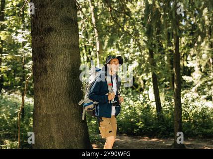 Senior man with backpack and hiking clothes walking in forest. Mature male enjoying the view while walking in forest. Stock Photo
