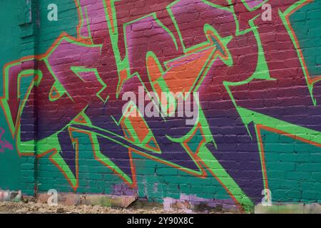 Creative graffiti artwork painted with green, orange, blue, purple and pink colors on wall of old brick building by skilled artist Stock Photo