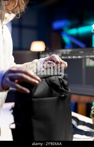 Admin packing backpack at end of day after securing company servers from virus attacks, close up. IT remote worker finishing job shift, leaving office after building firewalls protecting data Stock Photo