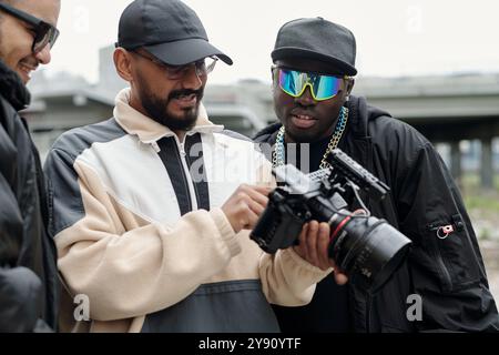 Group of filmmakers collaborating on film project, examining professional camera equipment and discussing scene by urban location enaged in creative process sharing ideas Stock Photo