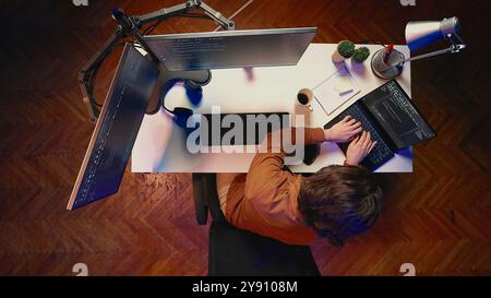 Top down view of hyperactive developer suffering from adhd, writing code, drinking coffee, listening music, arranging desk objects. Distracted IT admin doing multitasking in home office, aerial shot Stock Photo