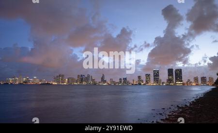 Pink light reflecting off clouds from sunset over the downtown city skyline of Miami behind the Atlantic Ocean Stock Photo