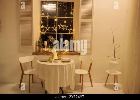 Cozy Christmas setting with a round table near the window, The table is decorated with a decorative Christmas tree in the center, Soft lighting from c Stock Photo