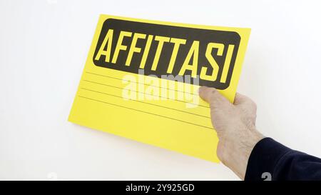 FOR RENT sign in Italian with yellow cardboard for writing, copy space and white background. Stock Photo