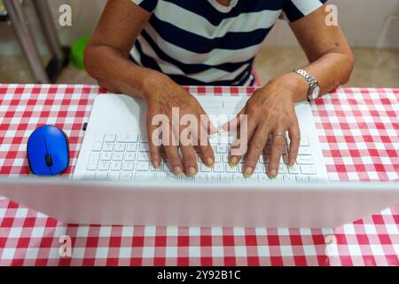 Elderly Hands Typing on Laptop Keyboard with Blue Mouse: Learning Technology at Home Stock Photo