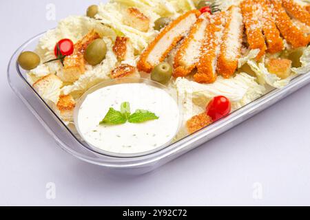 Crispy chicken salad with olives, cherry tomatoes, croutons, and creamy dressing in a clear bowl. Stock Photo