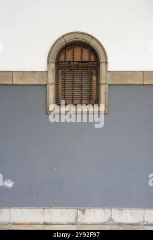 Arched window with wooden shutter on two-toned wall Stock Photo