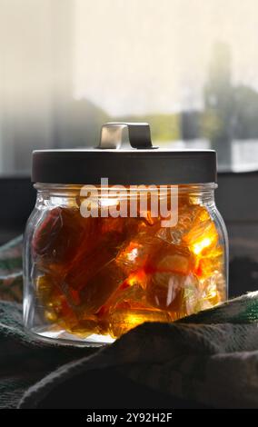 A jar of honey candies sits on a table. The candies are in a variety of shapes and sizes, and they are all yellow. The jar is made of glass and has a Stock Photo