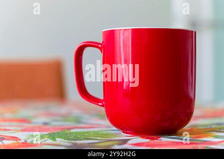 A red coffee cup sits on a table. There are sugar grains near the mug Stock Photo