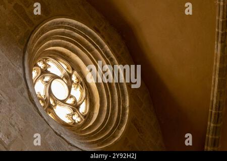 A window with a circular design is lit up by the sun. Gothic rose window. The light shines through the window, creating a warm and inviting atmosphere Stock Photo