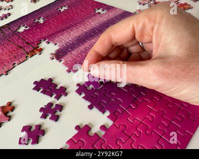 Doing a jigsaw puzzle close up showing hand and puzzle pieces Stock Photo