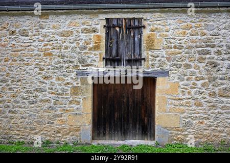 Old barn door with shuttered window above in a limestone wall Stock Photo