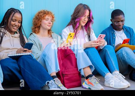 A group of diverse young people sitting outdoors using smartphones and notebooks Stock Photo