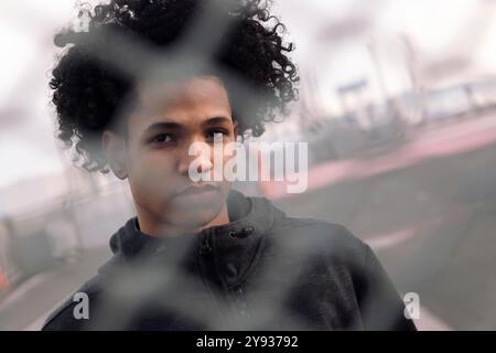 teen with curly hair behind metal chain link fence Stock Photo