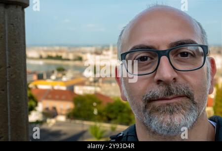 Budapest, Hungary, August 26, 2022. Portrait of a middle-aged Caucasian man with glasses. Behind him, a blurry view of the lower part of the city with Stock Photo