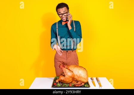 Photo of classy young man chatting phone look roasted thanksgiving turkey isolated on yellow color background Stock Photo