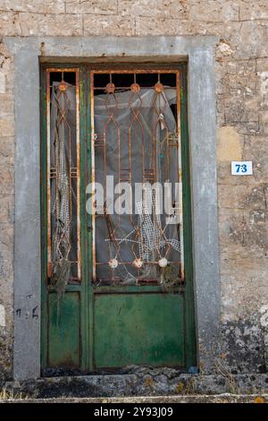 rusty old, green-painted doorway with ornate wrought iron panels on a derelict or abandoned building in Greece Stock Photo