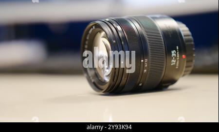 A close-up of a camera lens with detailed markings, resting on a reflective surface against a blurred background. This image highlights the precision Stock Photo