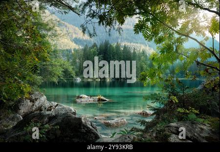 Idyllic view of a turquoise lake paradise in Bavaria, Germany. Tree branches and rocks frame the scene. Stock Photo