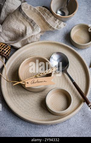 Elegant autumn table setting featuring ceramic plates, bowls, and cutlery, accented with a wheat stalk and a rustic Autumn tag Stock Photo