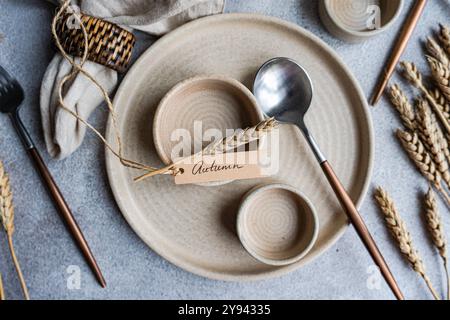 A cozy and stylish autumnal table setting features a wheat-themed decor, complemented by neutral-toned ceramic dishes and metallic flatware Stock Photo