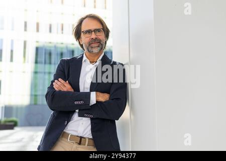 A confident middle-aged businessman standing with crossed arms in a modern urban setting, looking away. Stock Photo