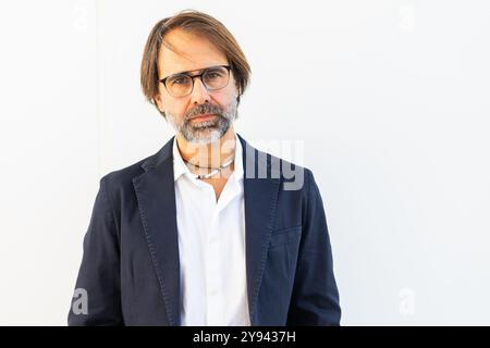 A mature male entrepreneur looks confidently at the camera, standing in an urban setting white background, wearing a suit and glasses. Stock Photo