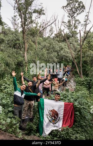 A spirited group of Mexican hikers waves and poses with a large Mexican flag amidst verdant trees in an outdoor nature setting, radiating unity and en Stock Photo
