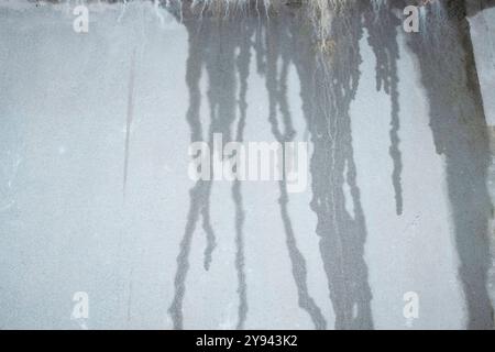 A stark grey concrete wall exhibits the minimalist aesthetics of brutalism with linear water streaks causing a natural, organic contrast. Stock Photo