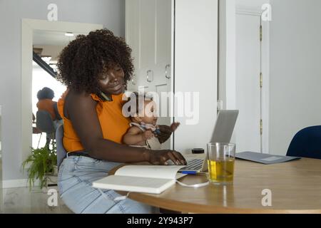 Loving African mom bonded with her baby while working on a laptop at home, showcasing a multiethnic family setup Stock Photo