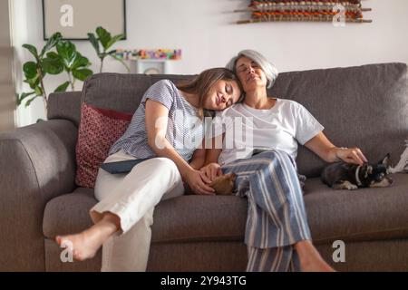 A serene moment portraying a mother and her daughter resting on a sofa, with both peacefully asleep and the daughter laying her head on her mother's s Stock Photo