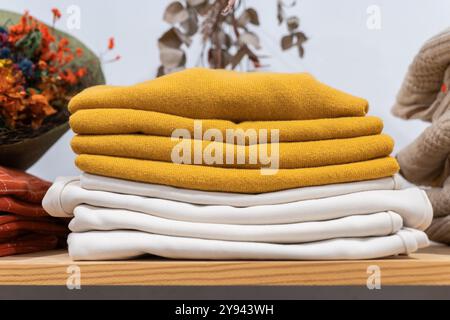 A stack of neatly folded sweaters in vibrant yellow and classic white hues laid on a wooden table, suggesting warmth and comfort Stock Photo