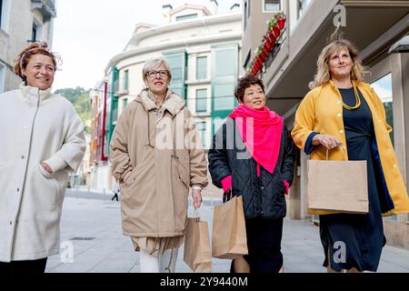 Four mature women enjoying a shopping spree, shown walking through a city street, each carrying shopping bags Stock Photo
