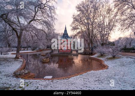 A picturesque view of a traditional Madrid building, La Casita del Pescador in Buen Retiro Park covered in snow, reflected in a nearby puddle of water Stock Photo