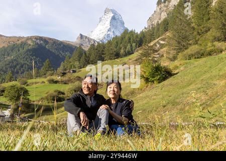 A cheerful Korean couple relaxes in Zermatt, Switzerland The iconic Matterhorn mountain stands majestically in the background, capturing the essence o Stock Photo