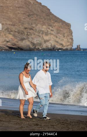 A young couple strolls along the shore of a sandy beach in autumn, with the waves crashing in the background Both dressed in white, they enjoy a quiet Stock Photo