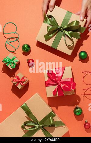 An arrangement of Christmas gifts in various sizes, each adorned with festive colorful ribbons on an orange background, placed by one person, capturin Stock Photo