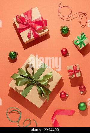 Colorful Christmas gifts adorned with red and green ribbons along with small ornament balls and coiling ribbon strands on a textured coral background, Stock Photo
