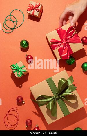 A tasteful display of Christmas presents wrapped with red and green ribbons, complemented by scattered ornaments on a vivid orange surface, capturing Stock Photo