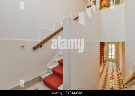 An elegant home interior featuring a white staircase with red carpet, checkered floor tiles, and bright natural light. Stock Photo