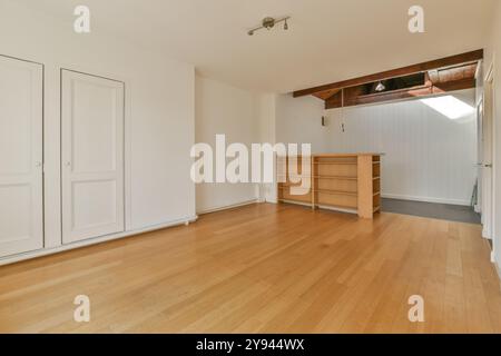 An empty room featuring a wooden floor, white walls, and a small wooden bookcase under a lofted area. Stock Photo