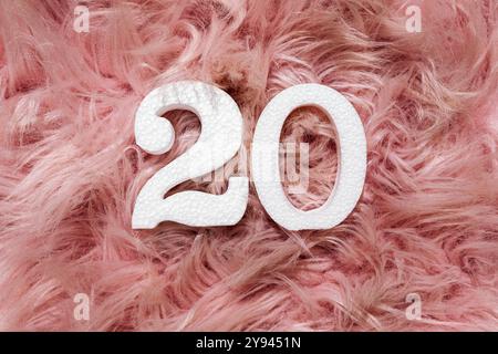 A creative display featuring a white textured number 20 resting on a soft, fluffy pink feather surface, perfect for concepts of age, celebration, and Stock Photo