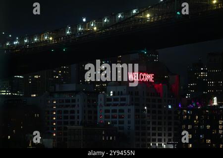 Nighttime view of an illuminated 'Welcome' sign on a building in Brooklyn. The dark scene is contrasted by city lights from the surrounding buildings Stock Photo