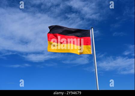 The flag of Germany flutters in the wind against a blue cloudless sky Stock Photo