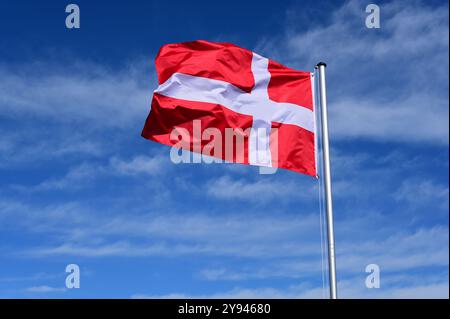 The flag of Denmark flutters in the wind against a blue cloudless sky Stock Photo