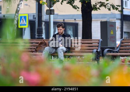 Man sitting with laptop on a bench in autumn city park. Working outdoor concept Stock Photo