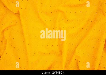 Bright yellow embroidered fabric with intricate eyelet design spread across, ideal for textile backgrounds and creative design projects Stock Photo