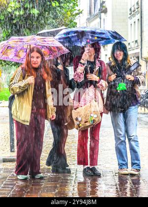 Four young women standing on street corner in pouring rain deciding where to go - Tours, Indre-et-Loire (37), France. Stock Photo